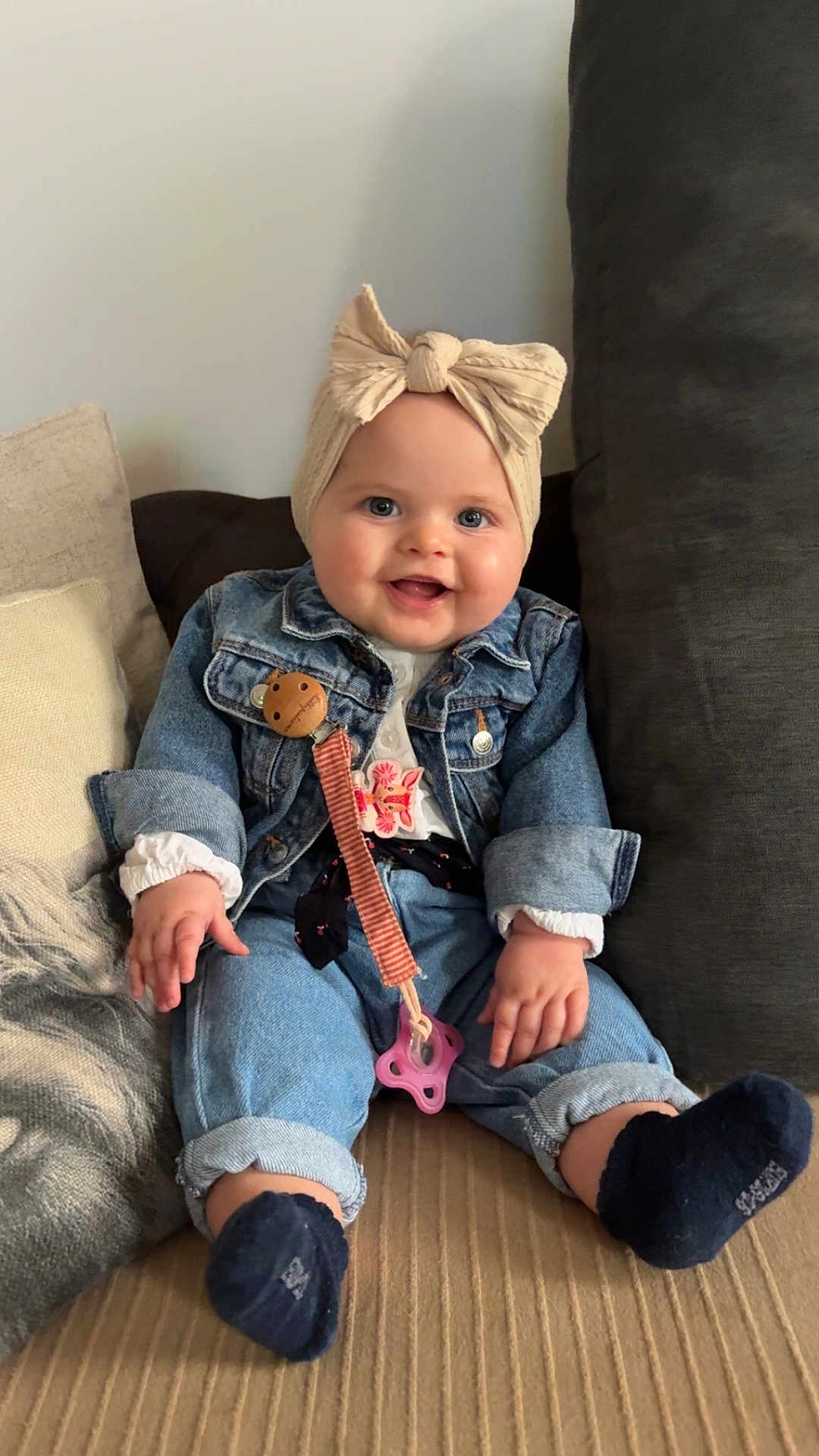 Tess participe au concours pour gagner de l'argent avec cette photo : baby, child, smiling, denim_jacket, headband, bow, pacifier_clip, couch, pillow, blue_eyes, socks, casual_clothing, indoor, happy, seated, infant, cute, portrait, cozy, hands