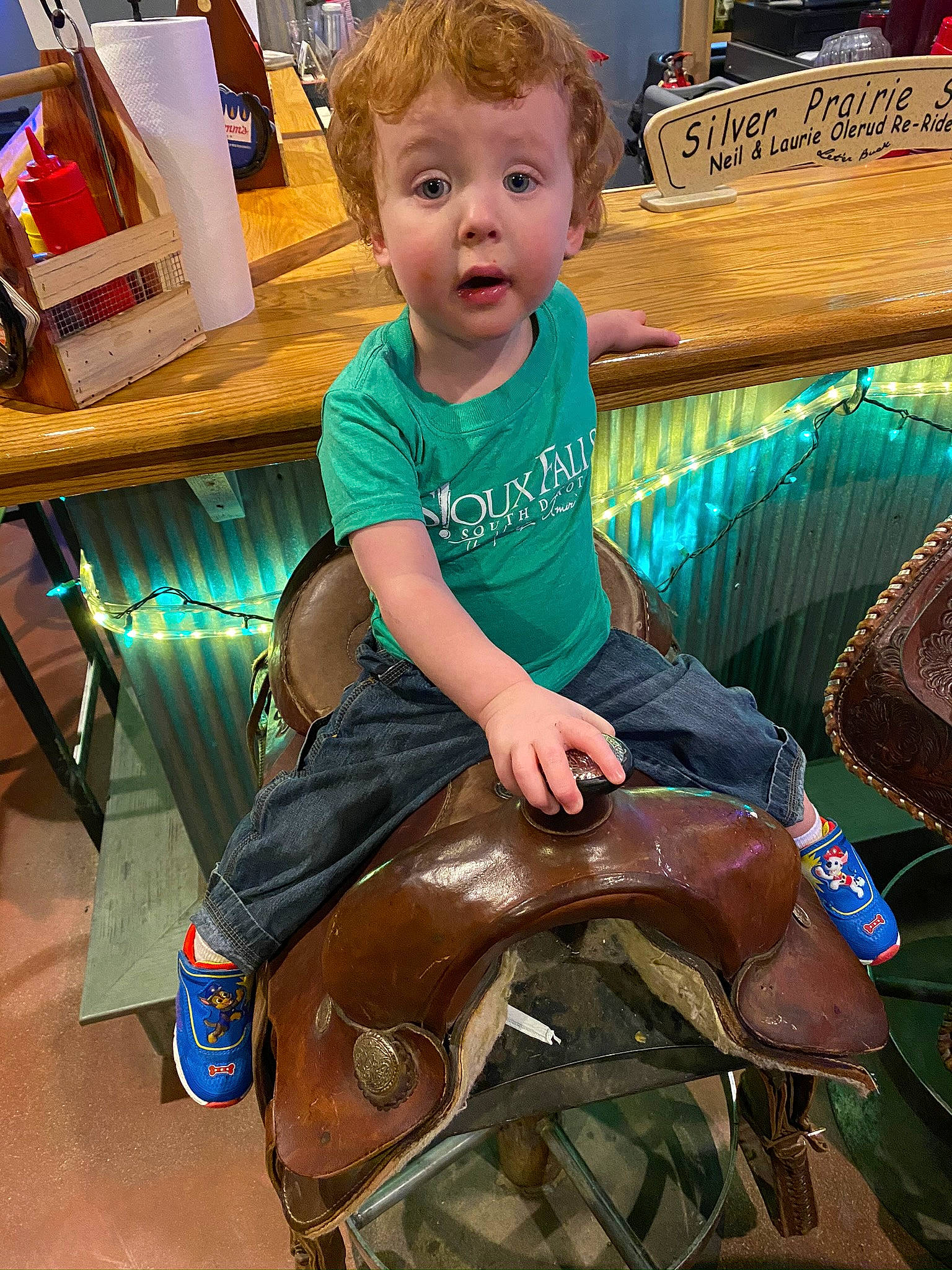 Thorin is registered to the contest to win money with this photo: chair, child, cool, event, fawn, fun, hairstyle, happy, head, human_leg, lap, leisure, person, recreation, sitting, smile, surprise, t_shirt, thigh, toddler