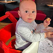 Mylan participe au concours pour gagner de l'argent avec cette photo : toddler, child, high_chair, red_chair, bread, snack, table, restaurant, activity_sheet, coloring, gray_sweater, face, eyes, hand, wooden_floor, seat, indoor, person, cute, portrait
