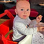 toddler, child, high_chair, red_chair, bread, snack, table, restaurant, activity_sheet, coloring, gray_sweater, face, eyes, hand, wooden_floor, seat, indoor, person, cute, portrait