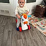 toddler, child, toy, indoor, pacifier, sunglasses, floor, play_mat, storage_basket, white_door, wooden_floor, clothing, person, baby, face, sitting, cute, room, plastic_toy, expression