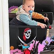 Mylan participe au concours pour gagner de l'argent avec cette photo : black_toy, blue_toy, casual_clothing, child, container, couch, curious, floor, foam_puzzle, hoodie, indoor, orange_toy, pacifier, person, pirate_skull, plastic_toy, red_toy, seated, toddler, toy