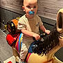 Mylan participe au concours pour gagner de l'argent avec cette photo : toddler, child, pacifier, indoor, mechanical_ride, horse_ride, colorful, toy, grip, blue_sneakers, light_clothing, wooden_wall, flooring, play_area, handlebars, cute, portrait, young_child, amusement_ride, focused