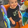 toddler, child, smiling, happy, sitting, amusement_park, carousel, ride, toy_horse, playground, indoor, portrait, black_shirt, shorts, colorful, plastic, background, family_outing, face, photography