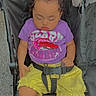 baby, buckle, calm, child, clothing, curly_hair, daylight, face, harness, infant, nap, outdoor, pavement, photography, portrait, purple_shirt, seated, sleeping, stroller, yellow_shorts