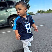 Eithan Dankiel Silva is registered to the contest to win money with this photo: accessory, asphalt, blue_sky, car, casual_clothing, child, curious_expression, daytime, football_jersey, gold_chain, outdoor, parking_lot, person, sneakers, standing, suv, tennessee_titans, toddler, tree, white_jeans