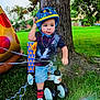 Eithan Dankiel Silva joined the competition — help win amazing prizes! birthday, casual_clothing, child, daylight, gift_box, grass, greenery, helmet, inflatable, outdoor, park, pizza, playing, shorts, sneakers, toddler, toy, tree, tricycle, tshirt