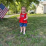 Oaklynne joined the competition — help win amazing prizes! toddler, child, flag, american_flag, red_shirt, denim_shorts, grass, outdoor, summer, daylight, trees, house, sidewalk, footwear, curly_hair, person, patriotic, portrait, standing, nature