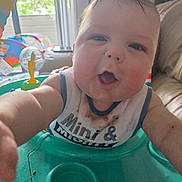 Hudson is registered to the contest to win money with this photo: baby, child, infant, face, bib, activity_seat, green, indoor, living_room, curious, reaching, cute, chubby, smiling, person, furniture, window, daylight, playful, clothing
