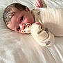 baby, infant, pacifier, milk_bottle, bed, sleepwear, animal_print, hand, face, eyes, lying_down, white_background, soft_texture, cute, newborn, child, comfort, cozy, rest, portrait