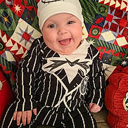 Xena is registered to the contest to win money with this photo: baby, smiling, child, hat, striped_clothing, couch, blanket, happy, portrait, indoors, face, person, infant, seated, cozy, cute, clothing, patterned, home, cheerful