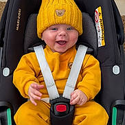 Freddie joined the competition — help win amazing prizes! baby, child, car_seat, yellow_clothing, knit_hat, teddy_bear_patch, smiling, happy, infant, straps, sitting, indoor, cute, face, person, seatbelt, safety, clothing, hood, car_seat_harness