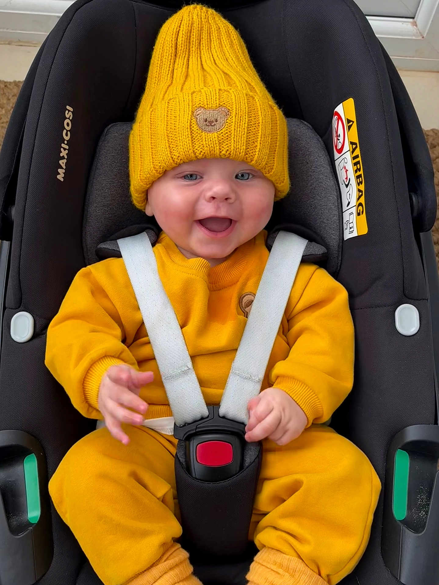 Freddie joined the competition — help win amazing prizes! baby, child, car_seat, yellow_clothing, knit_hat, teddy_bear_patch, smiling, happy, infant, straps, sitting, indoor, cute, face, person, seatbelt, safety, clothing, hood, car_seat_harness