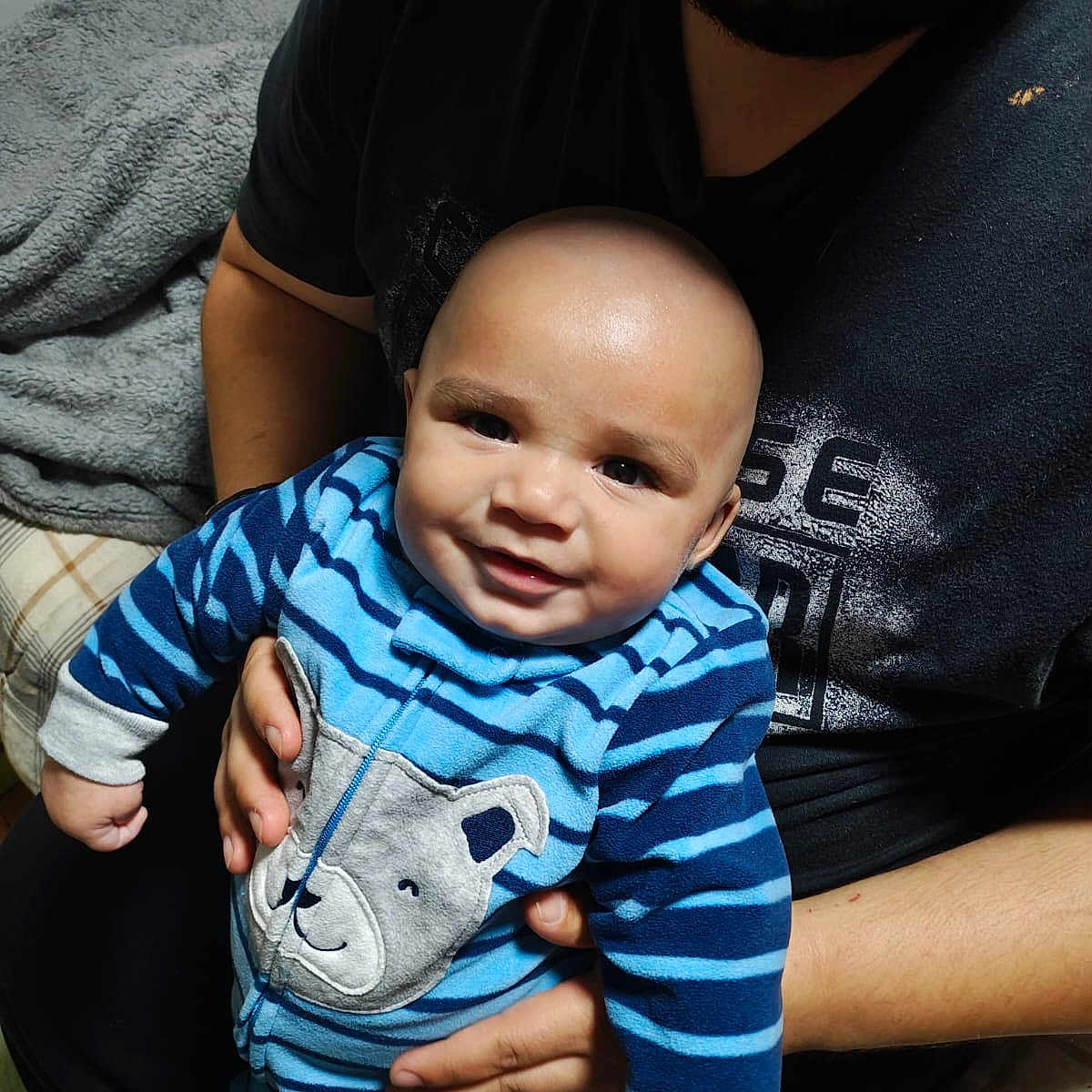 Levi is registered to the contest to win money with this photo: baby, child, infant, smiling, portrait, blue_outfit, striped_clothing, bear_patch, adult, parent, holding, family, indoor, home, blanket, couch, close_up, happy, cute, photograph