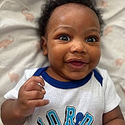 Giovanni joined the competition — help win amazing prizes! baby, smiling, happy, face, infant, clothing, tshirt, person, lying_down, cute, child, closeup, portrait, skin, hand, soft, blanket, animal_print, indoors, young