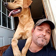 Troy Jones is registered to the contest to win money with this photo: animal, black_shirt, cap, casual, closeup, dog, door, facial_hair, friendship, glass_panes, happy, indoor, light, man, pet, portrait, shoulder, smile, tongue_out, window