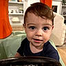 toddler, child, baby, portrait, face, eyes, brown_hair, smiling, high_chair, indoor, home, play_structure, orange, toy, steering_wheel, shirt, furniture, sitting, background, photograph