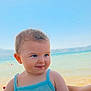baby, child, blue_clothing, beach, sea, sky, water, sunlight, smile, person, portrait, summer, vacation, holding, cute, outdoor, happy, skin, hand, nature