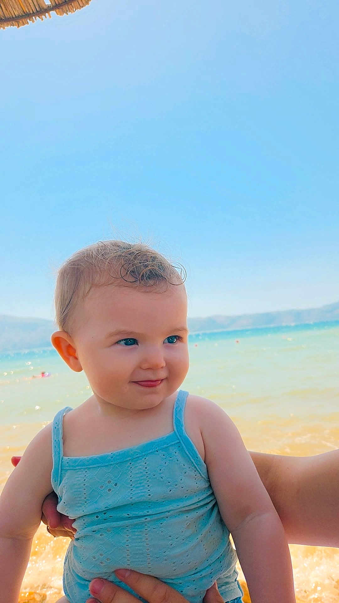 Leyna a rejoint le concours — aidez-le/la à gagner de superbes lots ! baby, child, blue_clothing, beach, sea, sky, water, sunlight, smile, person, portrait, summer, vacation, holding, cute, outdoor, happy, skin, hand, nature