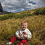 baby, child, grass, outdoor, nature, field, clouds, sky, hill, greenery, sitting, cute, sunlight, casual_clothing, red_pants, white_sweatshirt, person, young_child, curly_hair, daytime