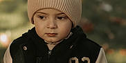 Egidio participe au concours pour gagner de l'argent avec cette photo : autumn, beanie, bokeh, child, cold_weather_clothing, eyes, face, fall_leaves, grass, jacket, knit_hat, number_patch, outdoor, portrait, serious_expression, shallow_depth_of_field, stylish_kid, varsity_jacket, warm_tones, young_child