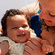 Oakleigh is registered to the contest to win money with this photo: baby, child, woman, smile, curly_hair, tattoo, blue_clothing, holding, happy, face, skin, portrait, closeup, person, love, family, affection, tenderness, warmth, sunlight
