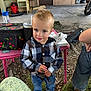 toddler, child, boy, plaid_shirt, jeans, sneakers, mohawk, blue_eyes, smile, outdoor, garage, table, bag, water_bottle, grass, rocks, person, clothing, curious, casual