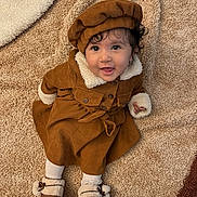 Mirella participe au concours pour gagner de l'argent avec cette photo : baby, child, smile, brown_clothing, hat, carpet, sitting, happy, indoors, footwear, coat, curly_hair, toddler, warm_clothing, cute, portrait, face, person, soft_texture, cozy