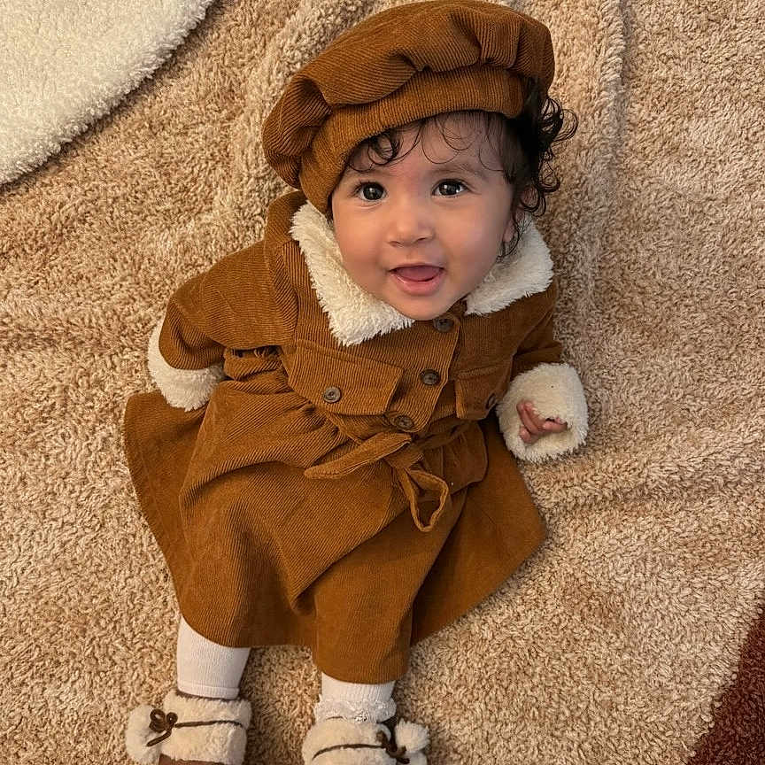 Mirella participe au concours pour gagner de l'argent avec cette photo : baby, brown_clothing, carpet, child, coat, cozy, curly_hair, cute, face, footwear, happy, hat, indoors, person, portrait, sitting, smile, soft_texture, toddler, warm_clothing