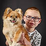 boy, child, pet, dog, pomeranian, fluffy, fur, glasses, portrait, studio, grey_background, smile, holding, sitting, t_shirt, jeans, happy, cute, hands, indoor