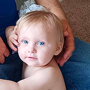 Kayden is registered to the contest to win money with this photo: toddler, child, blue_eyes, blonde_hair, face, portrait, skin, person, adult_hand, jeans, carpet, indoor, casual, close_up, candid, family, intimate, soft_light, expression, curious