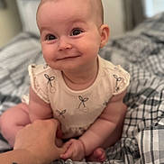 Elowyn joined the competition — help win amazing prizes! baby, child, smile, hand, plaid_blanket, sitting, cute, infant, person, skin, clothing, tattoo, bedroom, happy, expression, indoors, holding_hands, young, face, closeup