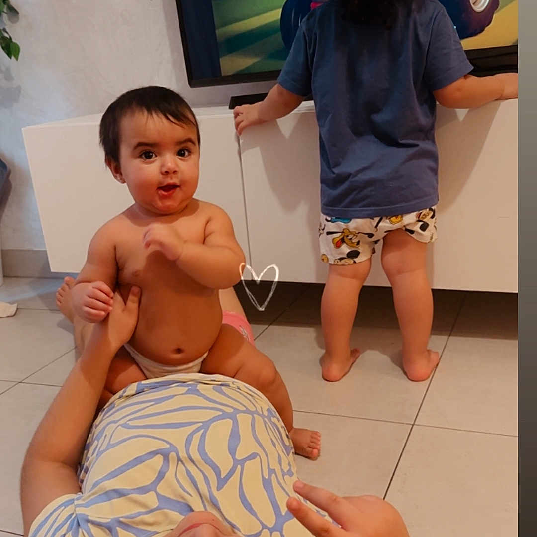 Charlotte a rejoint le concours — aidez-le/la à gagner de superbes lots ! baby, cabinet, cartoon, child, clothing, curly_hair, cute, family, footwear, hand_gesture, indoor, living_room, lying_down, peace_sign, person, playing, standing, television, tile_floor, toddler