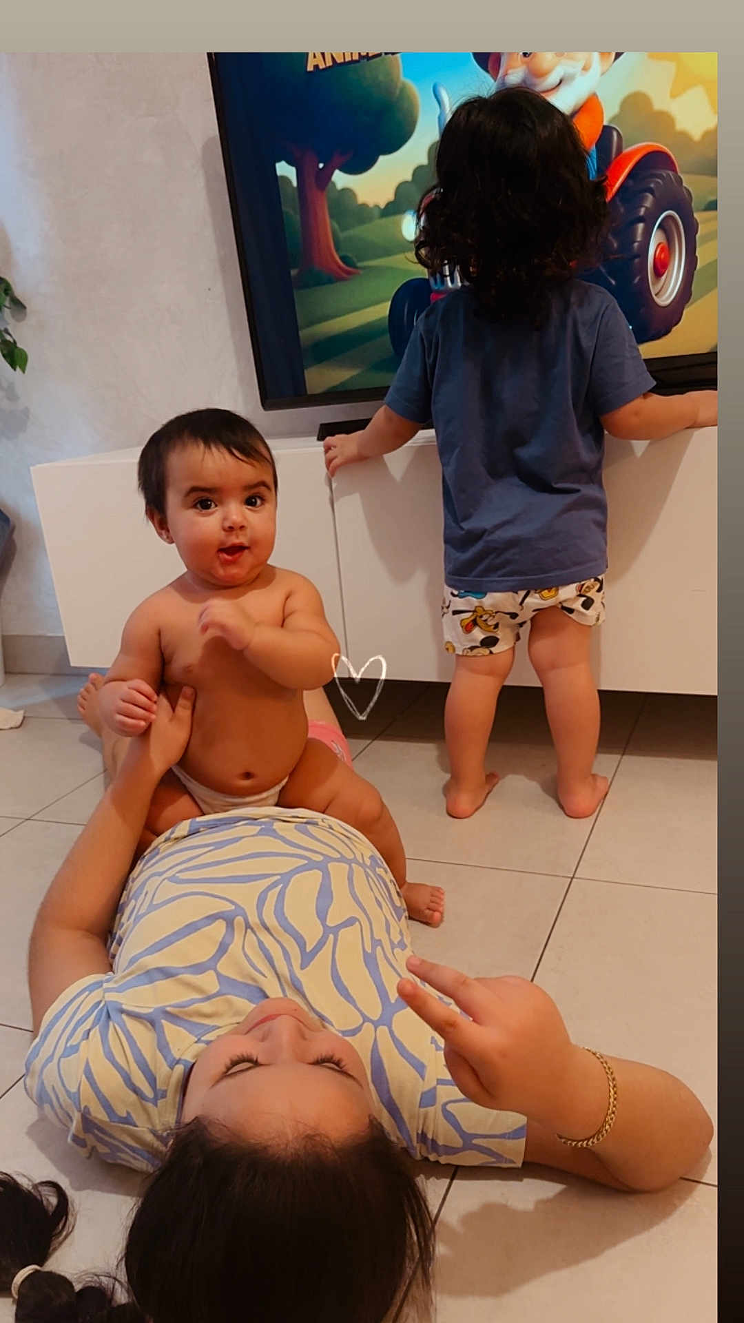 Charlotte a rejoint le concours — aidez-le/la à gagner de superbes lots ! baby, child, toddler, lying_down, standing, television, cartoon, living_room, tile_floor, clothing, peace_sign, curly_hair, playing, family, indoor, cabinet, footwear, hand_gesture, person, cute