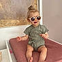 Cléa a rejoint le concours — aidez-le/la à gagner de superbes lots ! baby, child, sunglasses, romper, pink_cushion, indoor, smiling, sitting, top_knot, cute, fashionable, foot, hand, face, wooden_background, white_furniture, baby_clothing, infant, portrait, happy