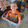 Joziyah is registered to the contest to win money with this photo: baby, blanket, cartoon, child, couch, furniture, happy, household_objects, indoor, laundry_basket, living_room, orange_shirt, paw_patrol, pillow, portrait, smiling, standing, tile_floor, toddler, toy