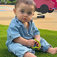 Roméo a rejoint le concours — aidez-le/la à gagner de superbes lots ! baby, child, grass, playground, toy, blue_outfit, barefoot, spring_rider, green_toy, outdoor, nature, curious, sitting, young_child, face, person, daylight, casual_clothing, park, play