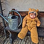 baby, child, bench, watering_can, rustic, outdoor, brown_clothing, fuzzy_suit, cute, expression, wood, stone_floor, hat_with_ears, cold_weather, winter_clothes, seated, portrait, one_person, young_child, cozy
