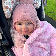Brooke is registered to the contest to win money with this photo: baby, child, pink_hat, knit_hat, pom_pom, blanket, fuzzy_blanket, stroller, floral_pattern, smiling, blue_eyes, cozy, outdoor, cute, person, infant, warm_clothing, happy, face, portrait