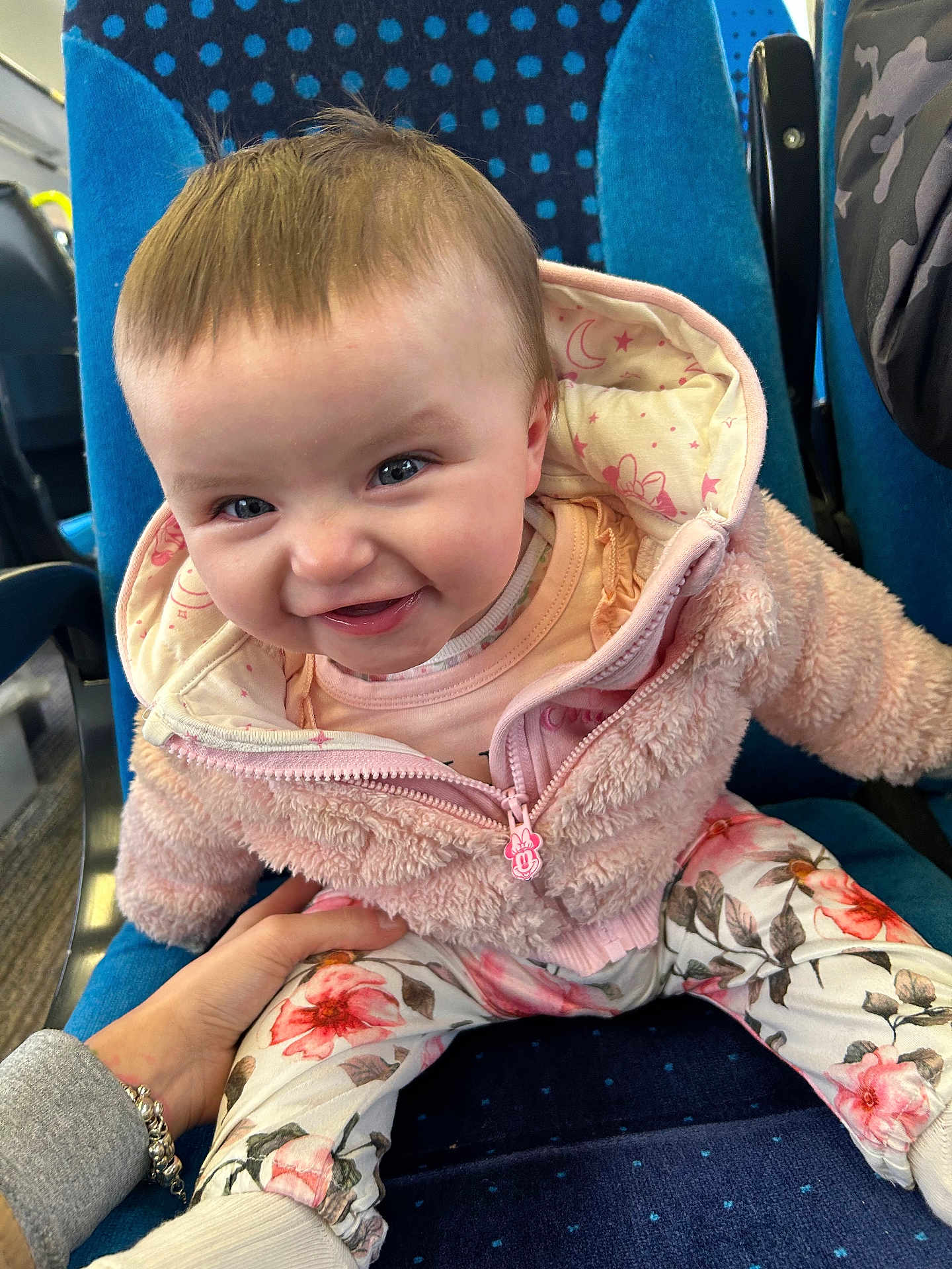 Brooke is registered to the contest to win money with this photo: baby, child, smiling, happy, pink_jacket, floral_pants, seat, hand, person, cute, indoor, clothing, portrait, young_child, face, sitting, blue_seat, warm_clothing, expression, infant