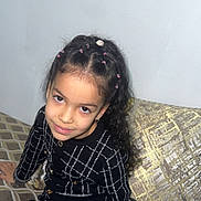 Widad participe au concours pour gagner de l'argent avec cette photo : child, girl, smiling, braided_hair, black_dress, patterned_dress, couch, cushion, indoor, seated, portrait, young, fashion, home, decor, gold_accent, white_socks, looking_at_camera, happy, casual