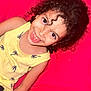 Widad participe au concours pour gagner de l'argent avec cette photo : child, smiling, curly_hair, yellow_tank_top, palm_tree_print, red_background, happy, portrait, face, person, casual_clothing, cute, young, joyful, indoor, skin, eyewear, earrings, expression, hair