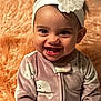 Jerrica Jay is registered to the contest to win money with this photo: baby, child, smiling, headband, flower, onesie, cozy, patterned_clothing, infant, happy, portrait, indoor, fuzzy_background, cute, young_child, face, tooth, sitting, closeup, warm_colors