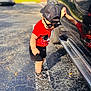 toddler, child, sunglasses, cap, red_shirt, black_shorts, sandals, car, reflection, parking_lot, asphalt, line_marking, leaf, sunlight, shadow, outdoor, person, casual_clothing, summer, playful