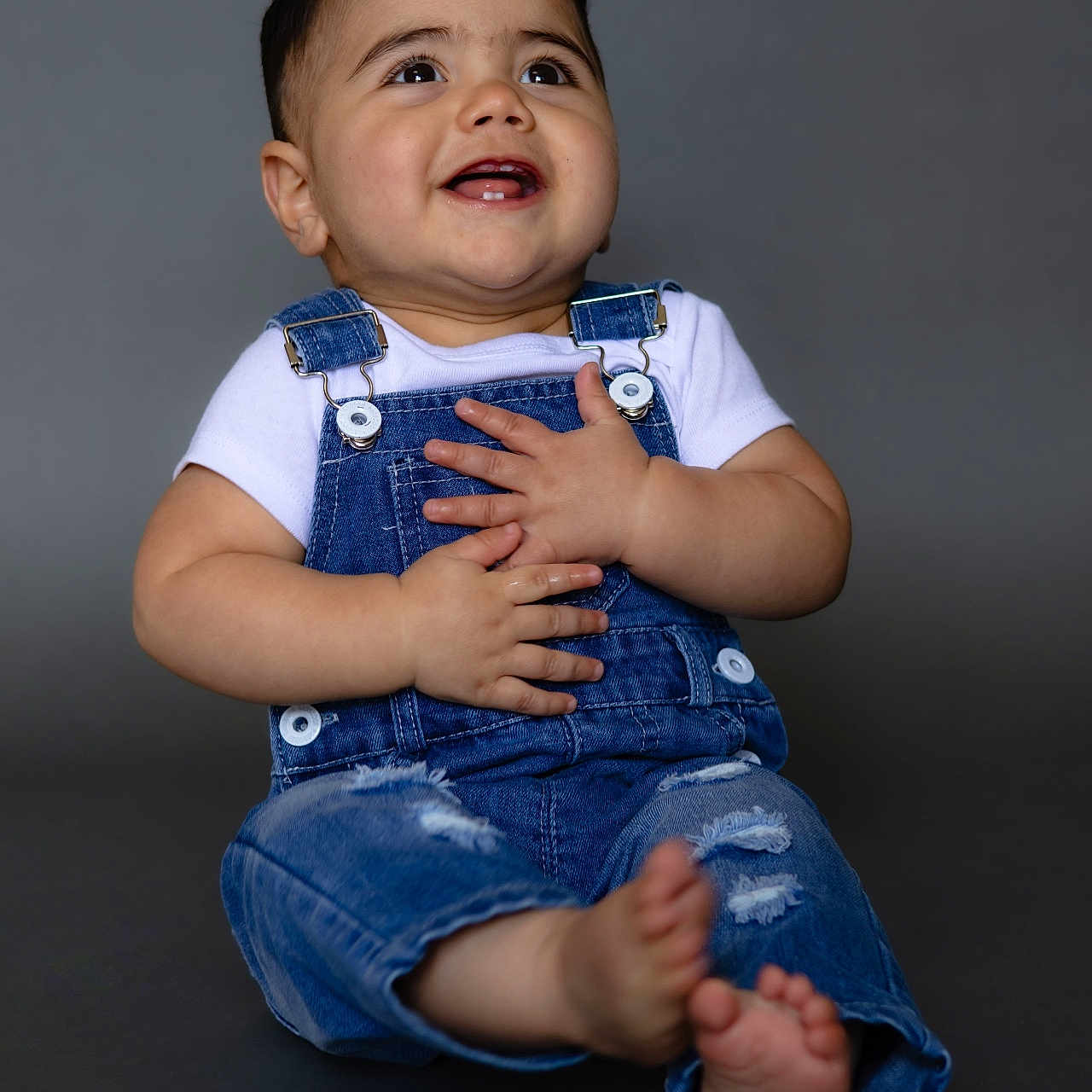 Bryan joined the competition — help win amazing prizes! baby, barefoot, casual_wear, child, cute, dark_background, denim_overalls, fashion, feet, hands, happy, isolated, portrait, sitting, smiling, spiky_hair, studio, toothy_grin, white_shirt, young_child
