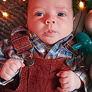 Axel joined the competition — help win amazing prizes! baby, infant, face, hands, clothing, overalls, plaid_shirt, pacifier, string_lights, holiday_decor, greenery, cozy, cute, indoors, portrait, expression, skin, eyes, fingers, warm_lighting