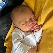 Zak is registered to the contest to win money with this photo: baby, newborn, sleeping, infant, person, hand, clothing, yellow_sweater, white_outfit, closeup, soft_lighting, portrait, indoor, resting, peaceful, human, skin, face, head, cozy