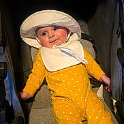 Miley is registered to the contest to win money with this photo: baby, child, smiling, yellow_outfit, white_hearts, hat, bib, stroller, infant, cute, happy, face, person, seated, clothing, portrait, rosy_cheeks, indoors, baby_fashion, closeup