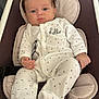 baby, infant, onesie, clothing, face, person, child, seat, baby_seat, padded_seat, white_onesie, stars_pattern, indoor, portrait, relaxed, cute, small_hands, footed_pajamas, expression, blue_eyes