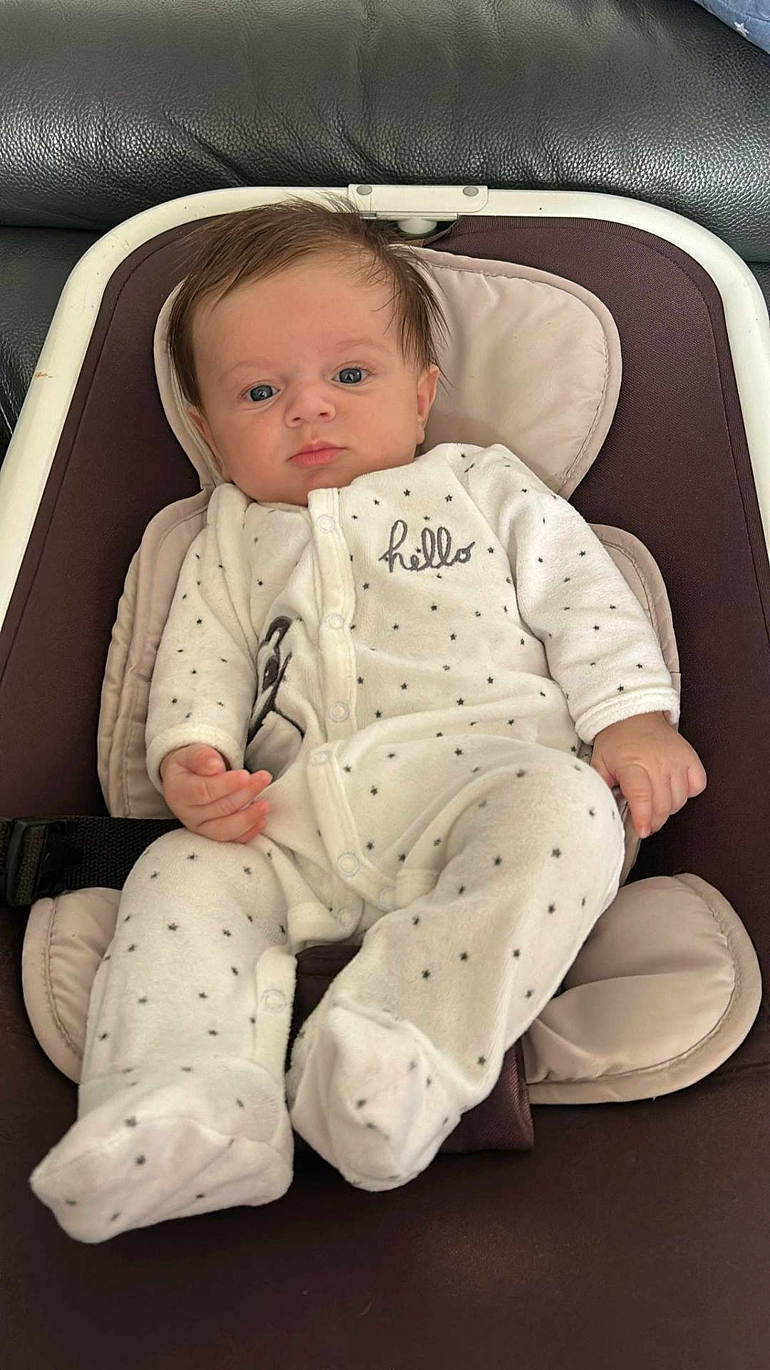 Nolan a rejoint le concours — aidez-le/la à gagner de superbes lots ! baby, infant, onesie, clothing, face, person, child, seat, baby_seat, padded_seat, white_onesie, stars_pattern, indoor, portrait, relaxed, cute, small_hands, footed_pajamas, expression, blue_eyes
